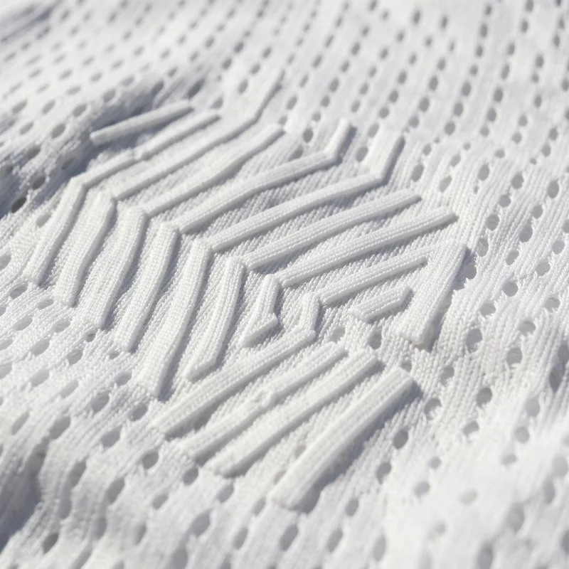 Gros plan sur un motif géométrique gaufré dans la maille blanche d’un maillot de sport
